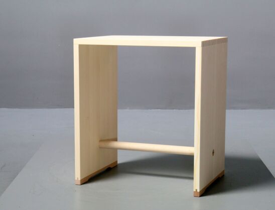 Der Ulmer Hocker ist aus Fichtenholz gearbeitet. Er hat eine Sitzfläche, einen Griff zum Tragen und kann auch auf die Seitenwange gestellt werden.